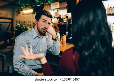 Girl Sitting In Front Of Young Guy And Talking To Him. He Looks Bored. Man Is Not Interested In Conversation At All.