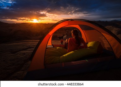 Girl Sitting inside orange tent looking at beautiful sunrise Lake Powell Reflection Canyon Utah USA
