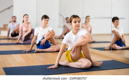 Girl sitting in lord of the fishes pose during group yoga training with her family in fitness studio.