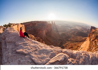 Girl sitting at the Mesa Arch at sunrise, Canyonlands National Park, Utah