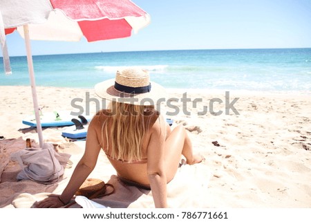 Girl sitting on beach under umbrella with straw hat sitting next to surf boards