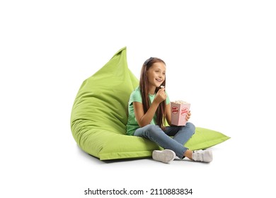 Girl sitting on a bean bag armchair with a box of popcorn and smiling isolated on white background
