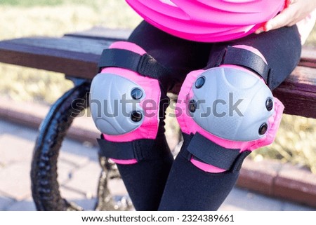 The girl is sitting on a bench in knee pads while riding a scooter. Protection of the knees from injuries when cycling and rollerblading.