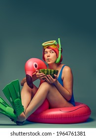 Girl sitting on big inflatable flamingo, ready to swim, blue studio background with empty space