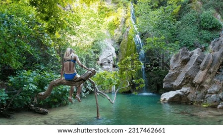 A girl sitting on a branch in the Richtis Gorge waterfall. It is a state protected park near Exo Mouliana, Sitia, eastern Crete. 