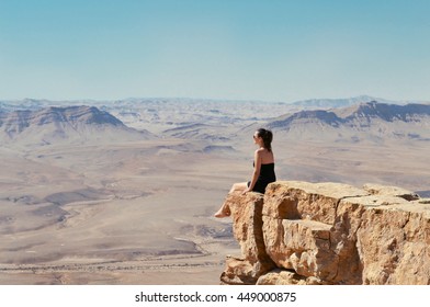 Girl sitting on a cliff and looking at desert Negev landscape. Summer vacation in Israel.