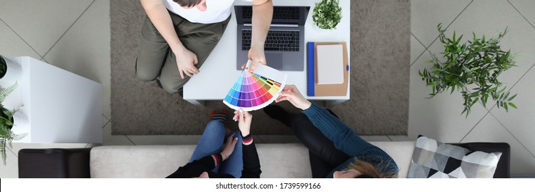 Girl are sitting on couch, man shows color palette. Girls choose color for painting walls in room. Guy suggests changing upholstery sofa, discussing future color. Psychological test