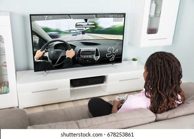 Girl Sitting On Couch Playing Video Racing Car Game At Home