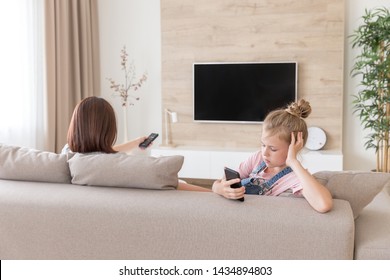 Girl Sitting On Couch And Watching Something Interesting In Mobile Phone While Mother Watching Tv