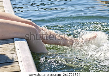 Girl sitting on dock splashing bare legs in lake