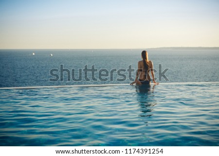 Girl is sitting on the edge of the pool and stare at the sea