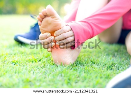 Girl sitting on green grass in the park. Foot pain from the wrong exercise .Symptoms of peripheral neuropathy. Most symptoms are numbness in the fingertips and foot. sun set light background.