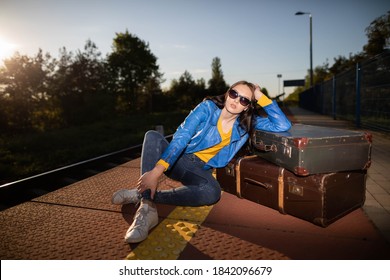 The girl is sitting on the platform of a railway station. Old travel suitcases. Boredom and fatigue while waiting for the train. - Shutterstock ID 1842096679