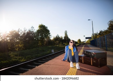The girl is sitting on the platform of a railway station. Old travel suitcases. Boredom and fatigue while waiting for the train. - Shutterstock ID 1842096682