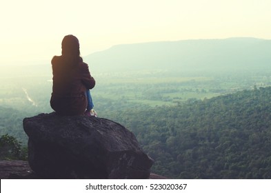 The girl sitting on the rock mountain , relaxing on the top of the mountain, silhouette