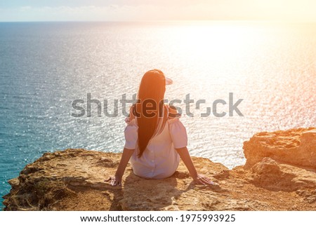 girl sitting on a rock. sun rays and glare. rejoices in freedom. beautiful cliff in the sea. back view. copy space.