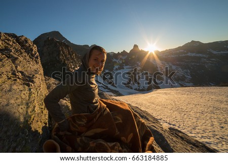 Girl sitting on a rock Watching Sunset From the top of the Mountain in a glacier area in the Alps with snow and blue sky