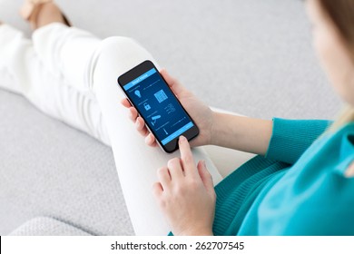 girl sitting on the sofa and holding a phone with program smart home on the screen - Powered by Shutterstock