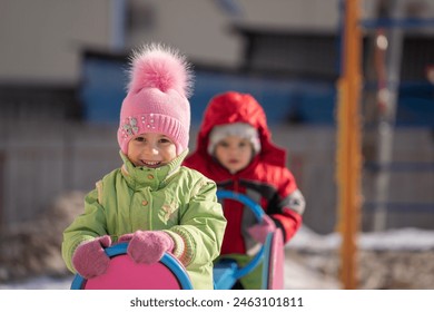 girl sitting on a swing in winter, winter fun, winter clothes, baby in winter, children - Powered by Shutterstock