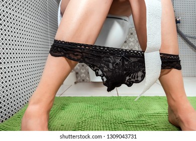 The girl sitting on the toilet holds toilet paper. The concept of problems with the chair, intestines, personal hygiene, constipation.