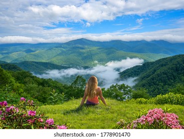 Girl Sitting On Top Of The Mountains Over The Clouds. Woman Looking At  Beautiful Summer Mountain View With Blooming Flowers. Near Asheville, Blue Ridge Mountains, North Carolina, USA.