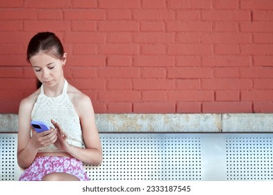 A girl is sitting on a train station bench and using her phone - Powered by Shutterstock