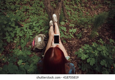 Girl sitting on a tree with her cell phone in the forest. Gadget concept. Travel concept.
