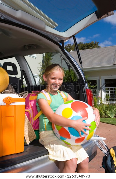 Girl sitting in open boot of car packed with\
luggage for vacation