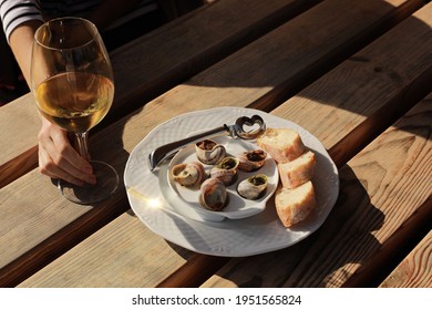 Girl sitting in outdoor cafe enjoying escargot snails with herbs butter and white wine.