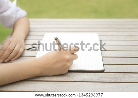 girl sitting outdoor and writing,Sit and write work in the garden,close up hand female are sitting using pen writing Record Lecture notepad into the book in the garden.