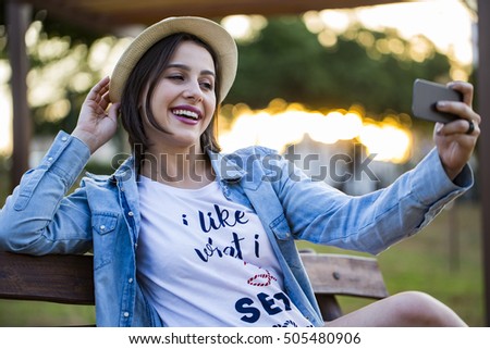 Girl sitting in the park and makes selfie, happy.