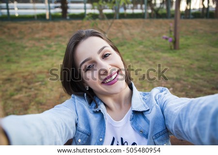 Girl sitting in the park and makes selfie, happy.