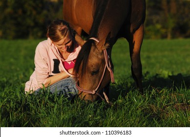 a girl sitting in the pasture beside her grazing horse