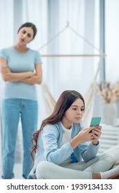 Girl Sitting With Smartphone And Mom Standing Behind