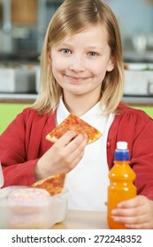 Girl Sitting At Table In School Cafeteria Eating Unhealthy Packed Lunch