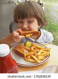 Girl Sitting At The Table Of A Street Cafe And Eating Grilled Cheese And French Fries.