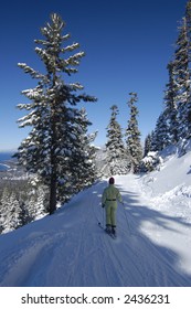 A Girl Is Skiing At Lake Tahoe Ski Resort Among Snow Covered Pines With Lake Itself In The Background.