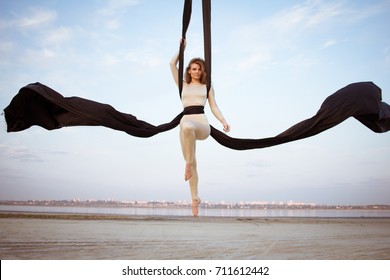 girl in skinny wear performing a dance on the black ribbons against the sky,  gymnast performing aerial exercise 