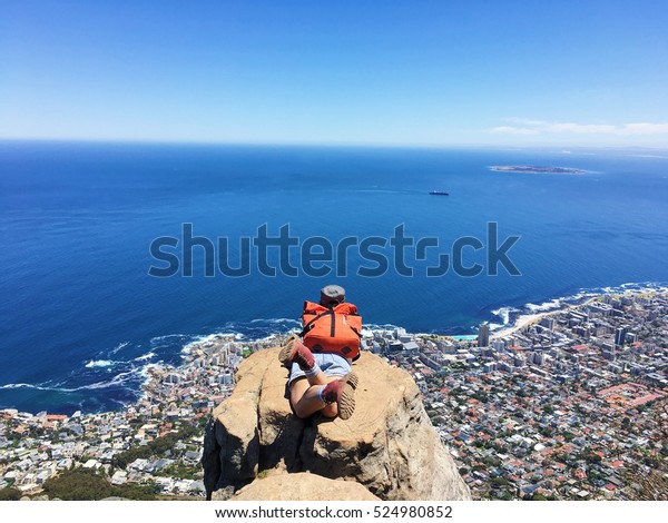 A girl sleep on a rock on top of Lion\'s head\
mountain overlooking the city and dark blue sea below with blue sky\
in Cape Town South Afica.