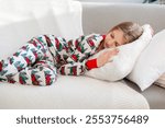 Girl sleeping on a cozy couch in festive pajamas. A young girl peacefully sleeping on a soft white pillow and blanket on a couch, dressed in festive pajamas.