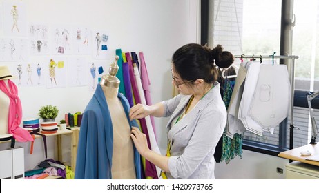 girl in smart casual shirt working in workshop studio. fashion designer female worker makes fitting on blue scarf on the mannequin. young asian woman with dummy designing new collection for summer