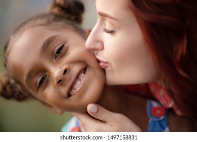 Girl smiling broadly. African-American adopted girl smiling broadly while mother kissing her