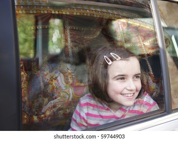 Girl Smiling And Looking Out Of Car Window At Fairground Ride With Reflection Of Carousel In Glass