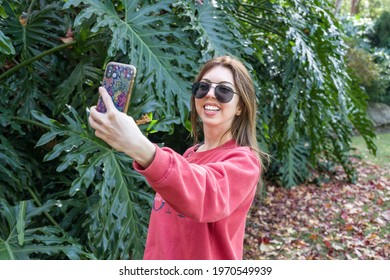 Girl smiling taking a selfie outdoors in the park with a garden plant backdrop