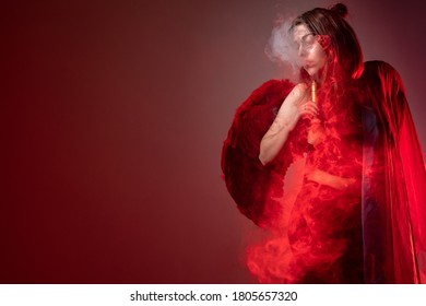 The girl smokes a VAPE. The concept of vaping in red. The girl lets out smoke from an electronic cigarette. Place for text. VAPE shop. A woman with an e-cigarette.