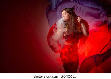 A girl smokes a VAPE on a red background. Vaping concept with space for your text. A girl blows out smoke from an e-cigarette and poses for the camera. Accessories for vaping in a VAPE shop.