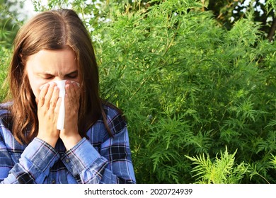 The Girl Sneezes Against The Background Of Ragweed. Ambrosia Pollen Allergy Concept.