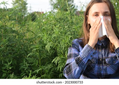 The Girl Sneezes Against The Background Of Ragweed. Ambrosia Pollen Allergy Concept.