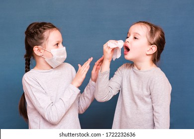 Girl Sneezes Hiding Behind A Handkerchief. The Second Girl Protects Herself From Her With A Mask And Hands. Infecting Children