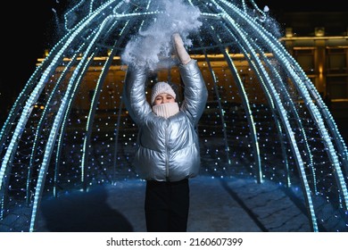 Girl and snow. Smiling girl in warm clothes throws snow outdoors at night with blue backlight. Christmas and New Year theme